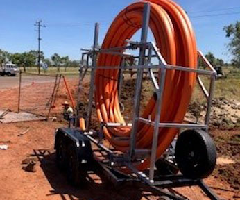 Pipe installation project in progress, featuring a mobile trailer loaded with coiled conduit for underground utility work.